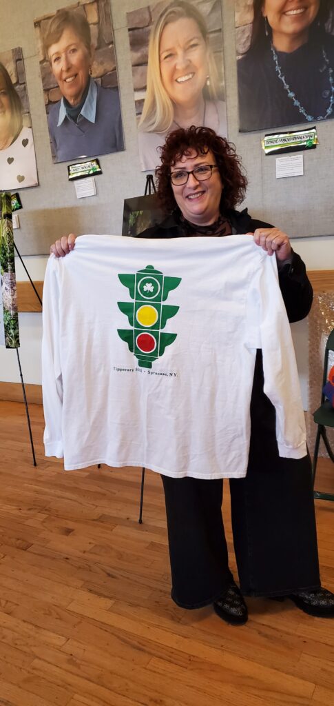 Kathleen holds up a long-sleeved T-shirt with the Tipperary Hill traffic signal (the colors are reversed)